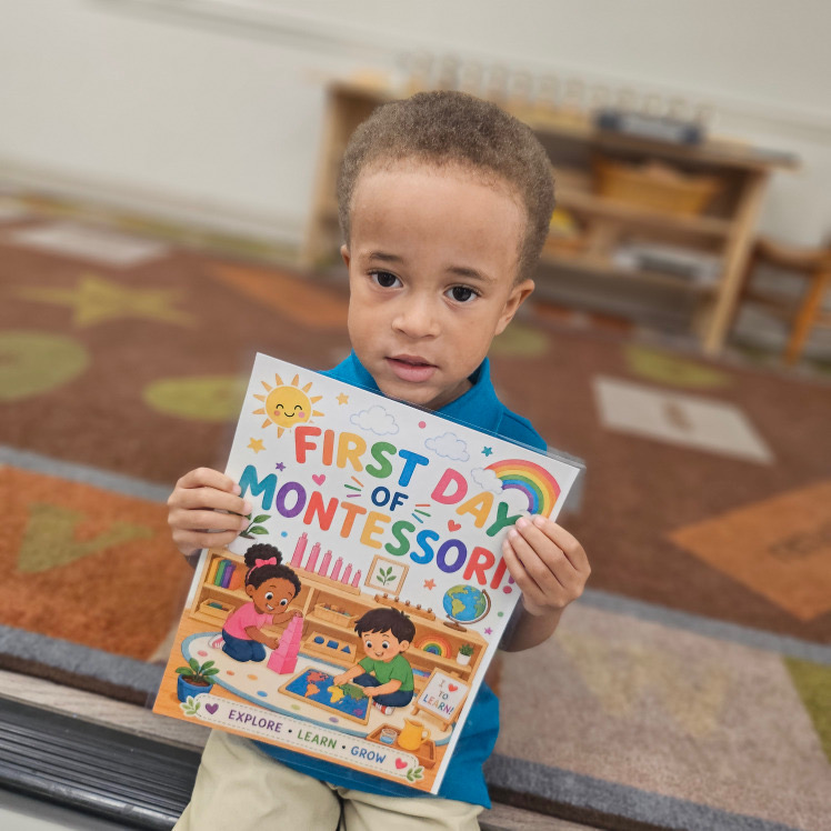 A young child holding a First Day of Montessori picture book